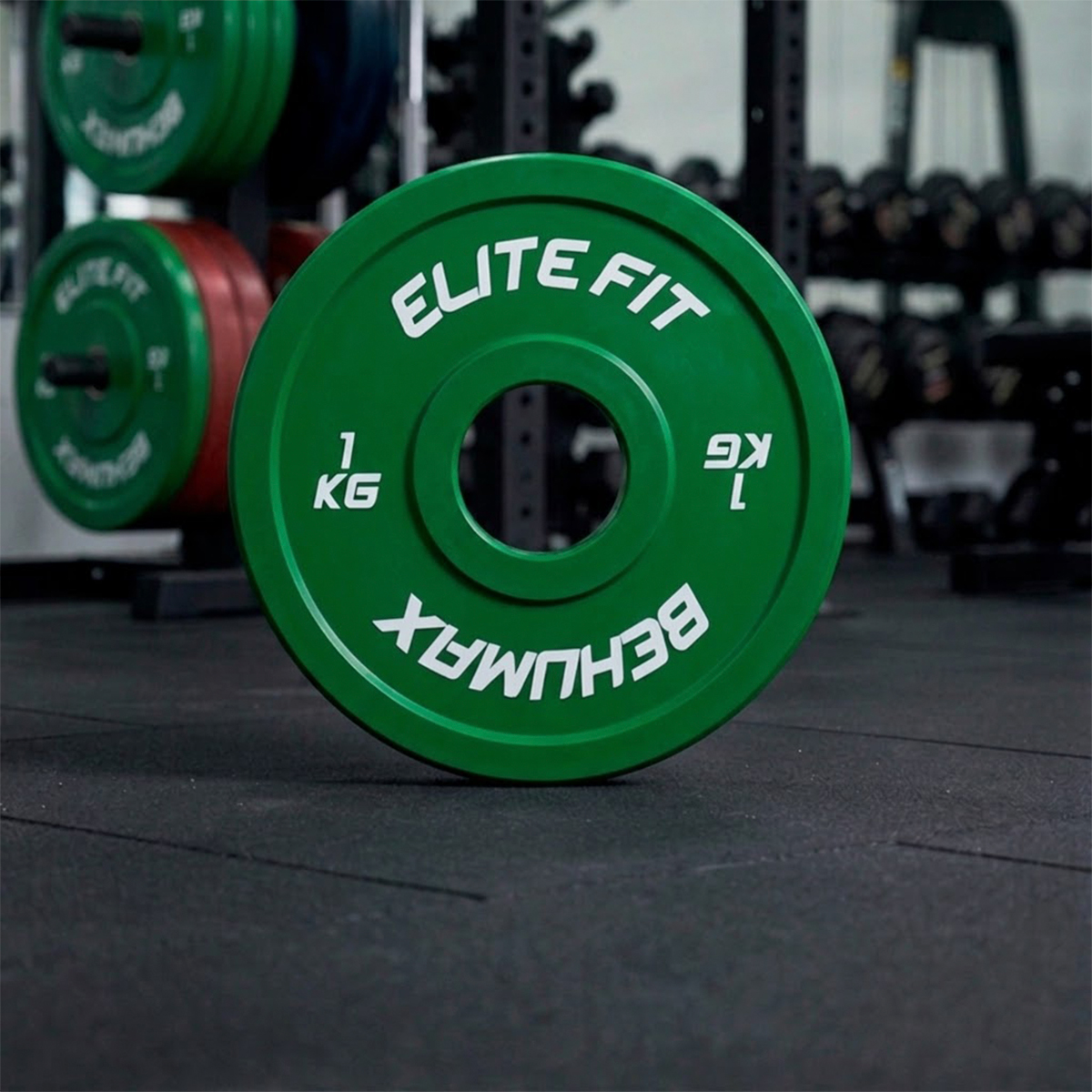 Un disco de pesas verde con texto blanco de ELITE FIT está de pie en el suelo de un gimnasio.