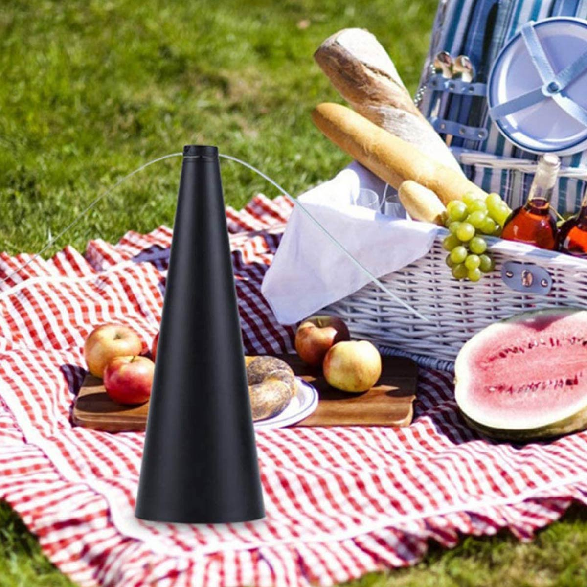 Schwarzer Tischventilator auf einer rot-weißen Picknickdecke mit Brotkorb, Obst und Wassermelone.