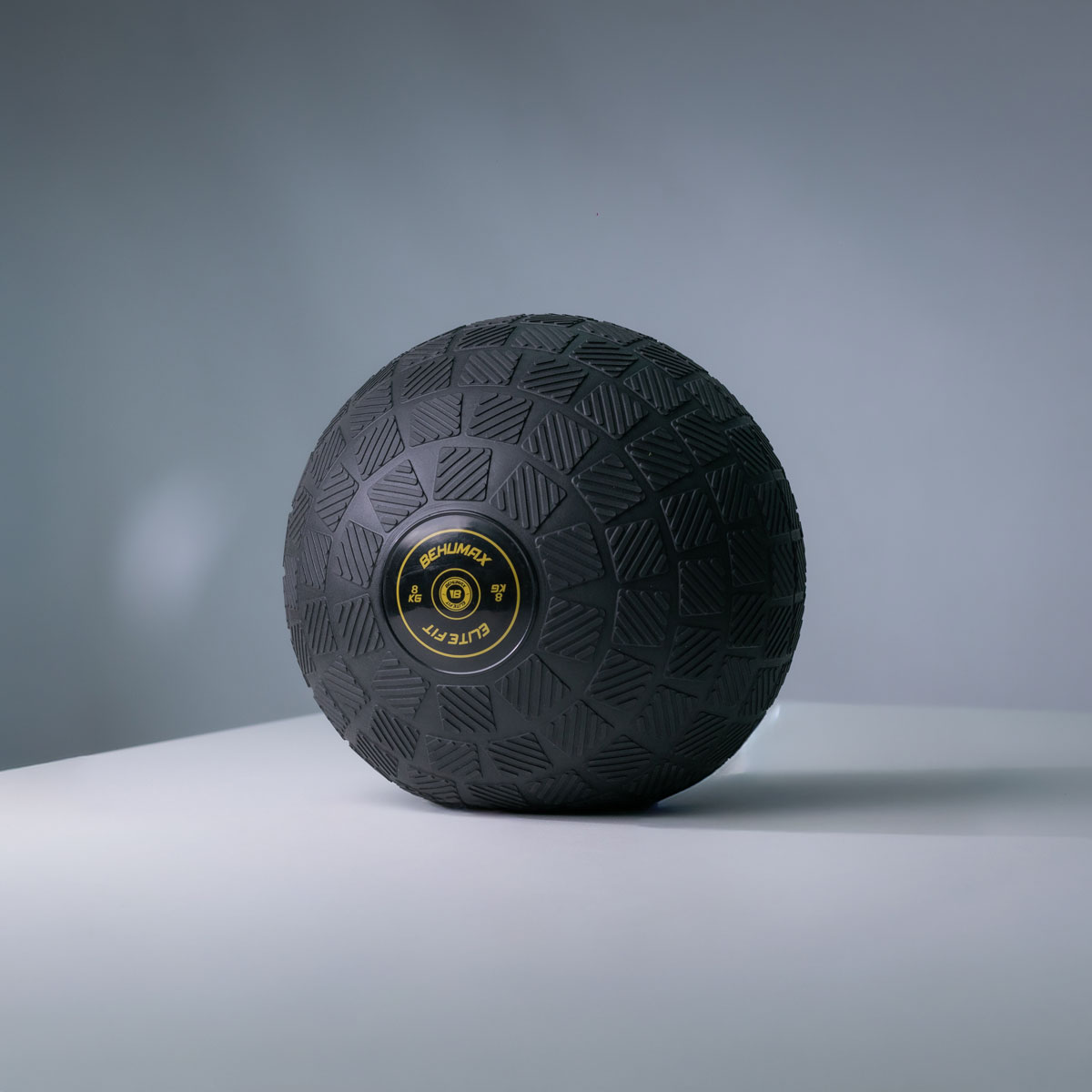 Un balón medicinal negro con patrón texturizado sobre una superficie clara con fondo gris.
