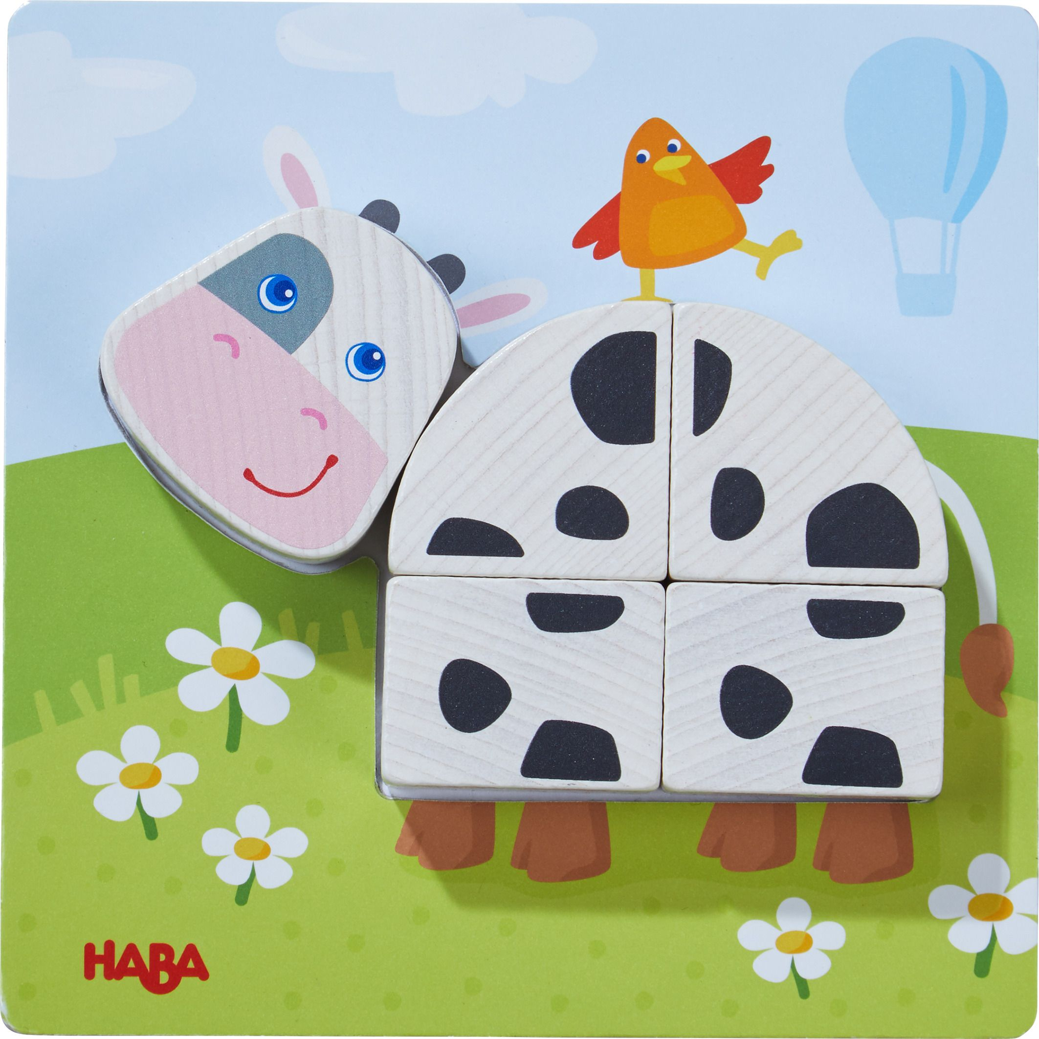 Ein Holzkuh-Puzzle auf grünem Wiesenboden mit einem kleinen orangefarbenen Vogel oben.