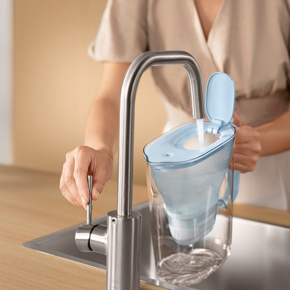 Una persona riempie una caraffa filtrante azzurra con l'acqua di un rubinetto moderno.