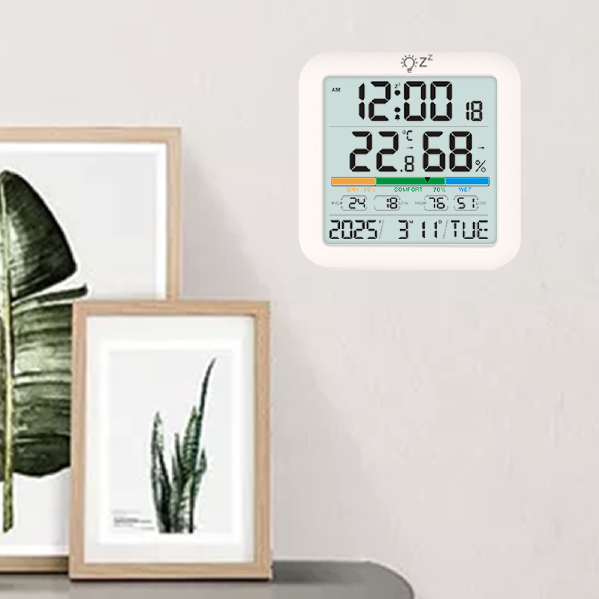 Digitale Uhr mit Temperatur- und Feuchtigkeitsanzeige an einer Wand neben gerahmten Bildern.
