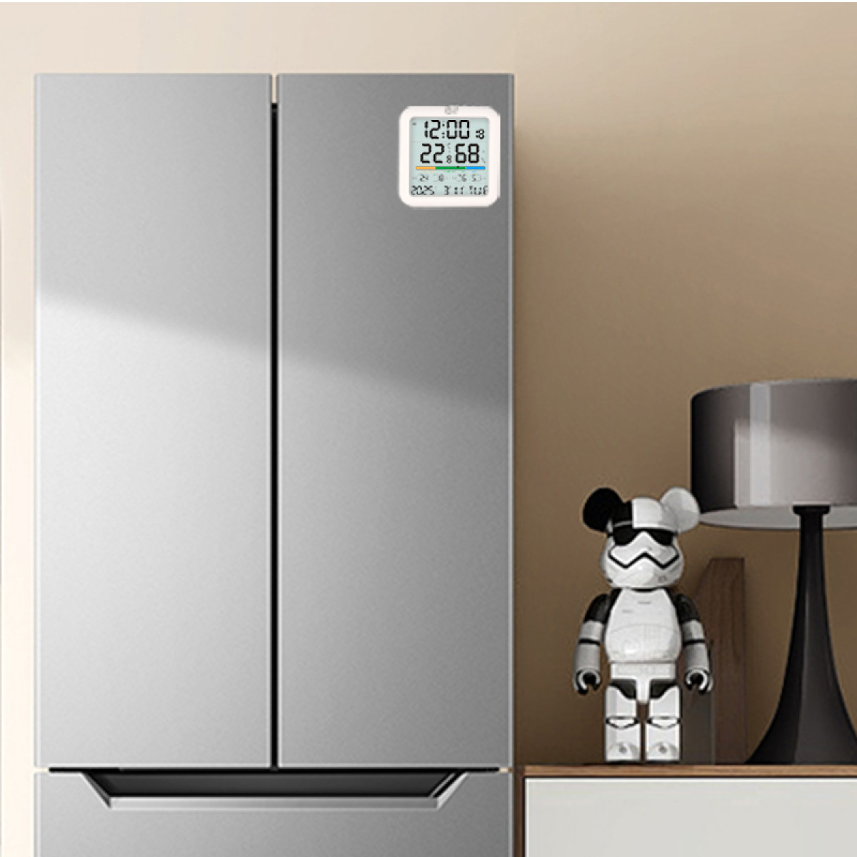 Eine Digitaluhr an einem silbernen Kühlschrank neben einer kleinen Spielfigur und einer Lampe.