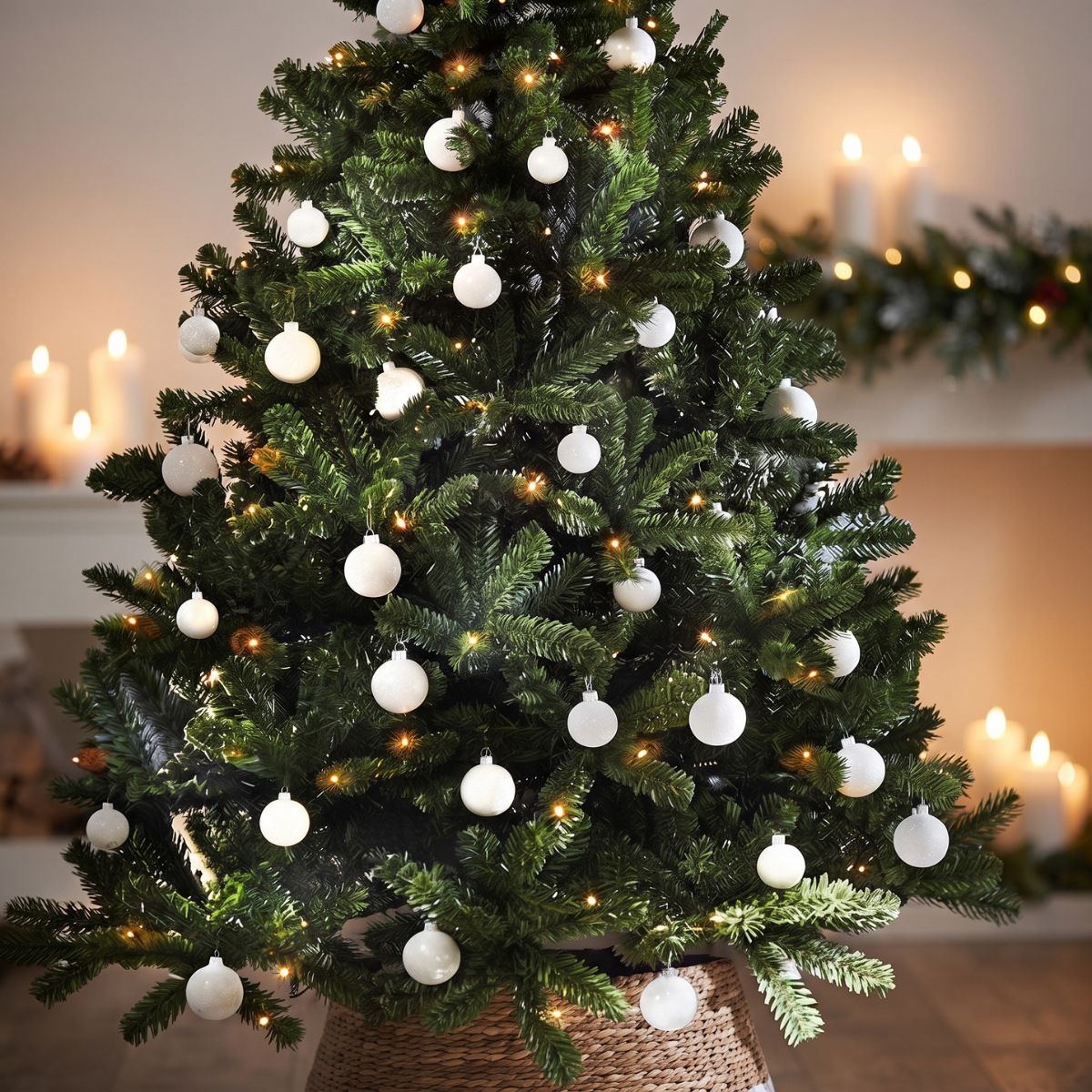 Een versierde kerstboom met witte kerstballen en lampjes staat in een kamer met brandende kaarsen.