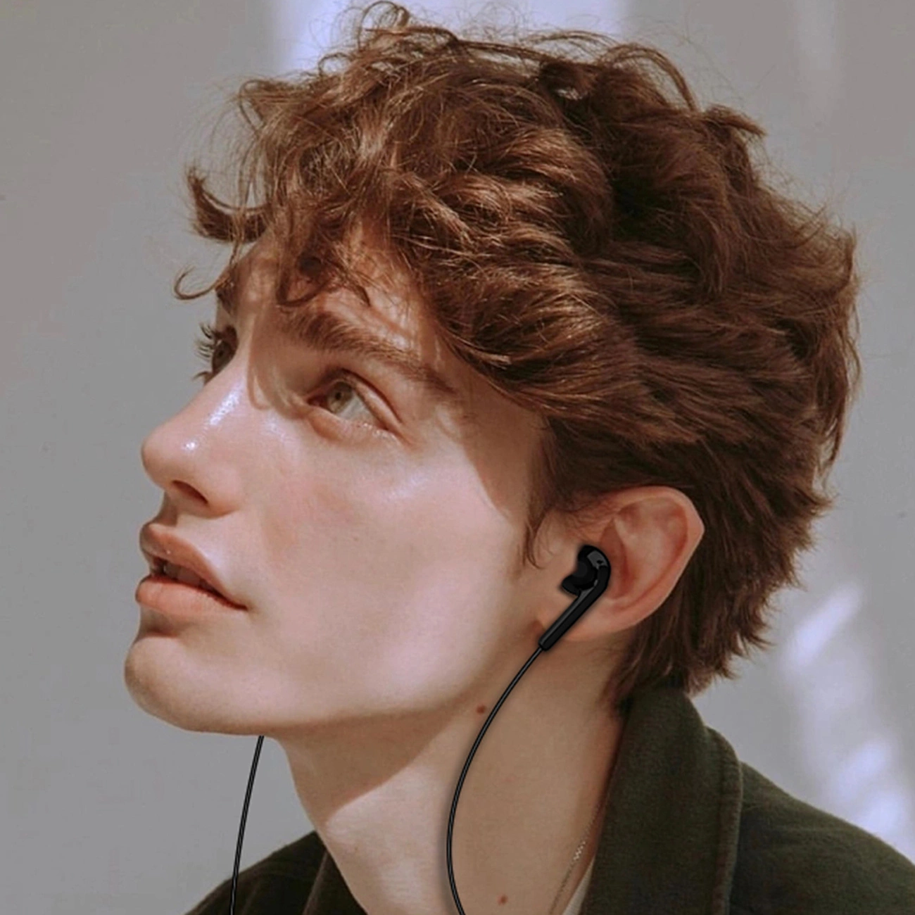 Un giovane con i capelli castani ricci guarda in alto indossando auricolari neri.