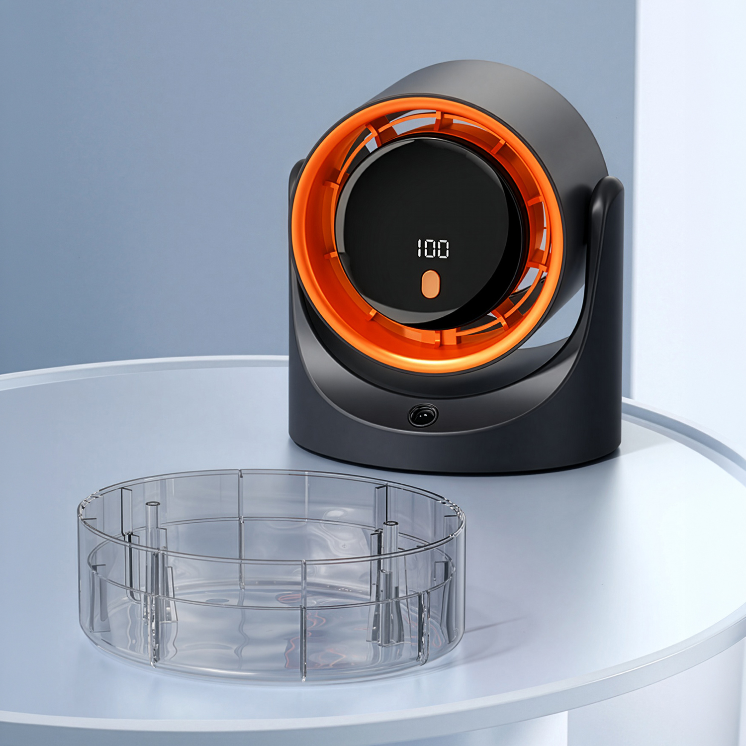 Un ventilador negro con un anillo naranja y pantalla digital sobre una mesa al lado de un bol transparente.