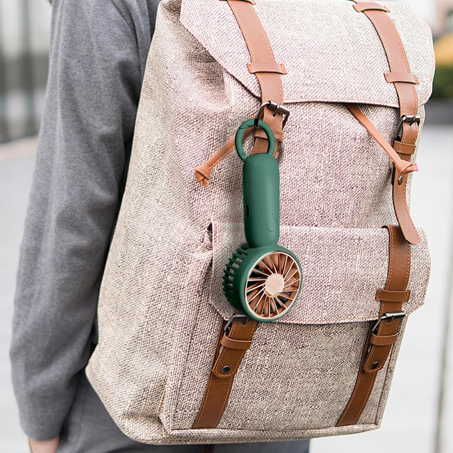 Ein kleiner grüner Handventilator hängt am Riemen eines beigen Rucksacks mit braunen Lederriemen.