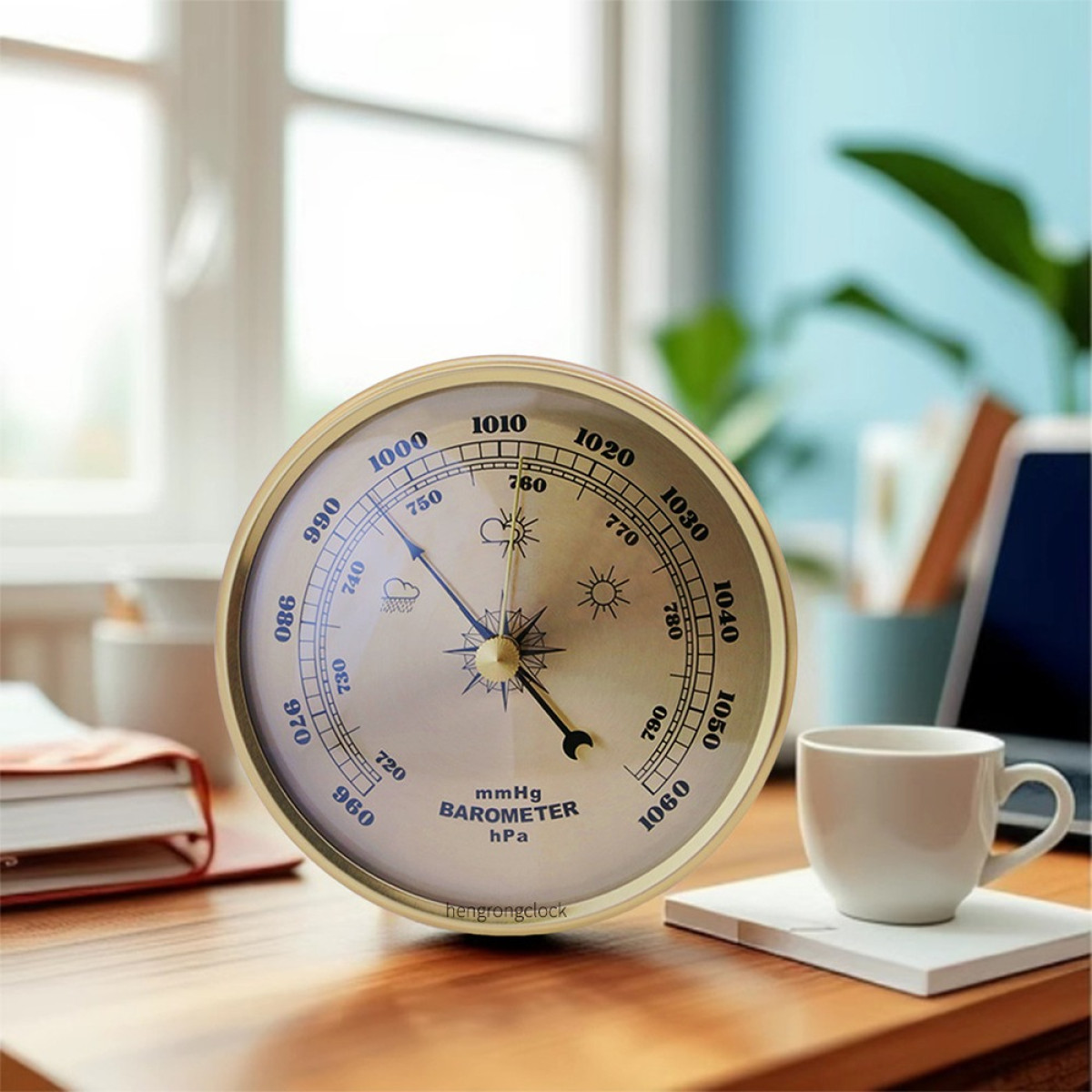 Ein Messing-Barometer steht auf einem Holzschreibtisch mit einer weißen Kaffeetasse und Büchern vor einem Fenster.