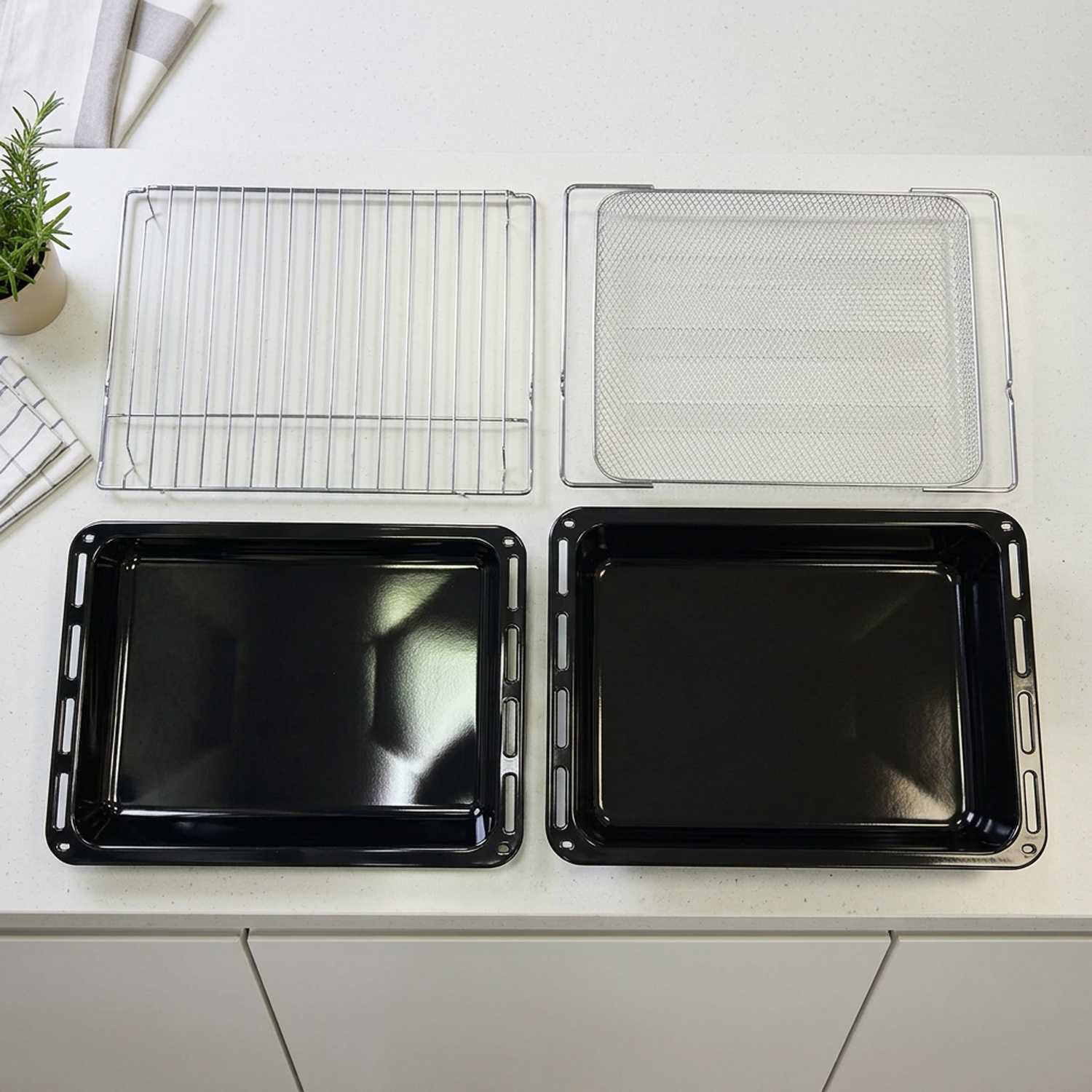 Zwei schwarze Backbleche und zwei silberne Roste liegen auf einer weißen Küchentheke.
