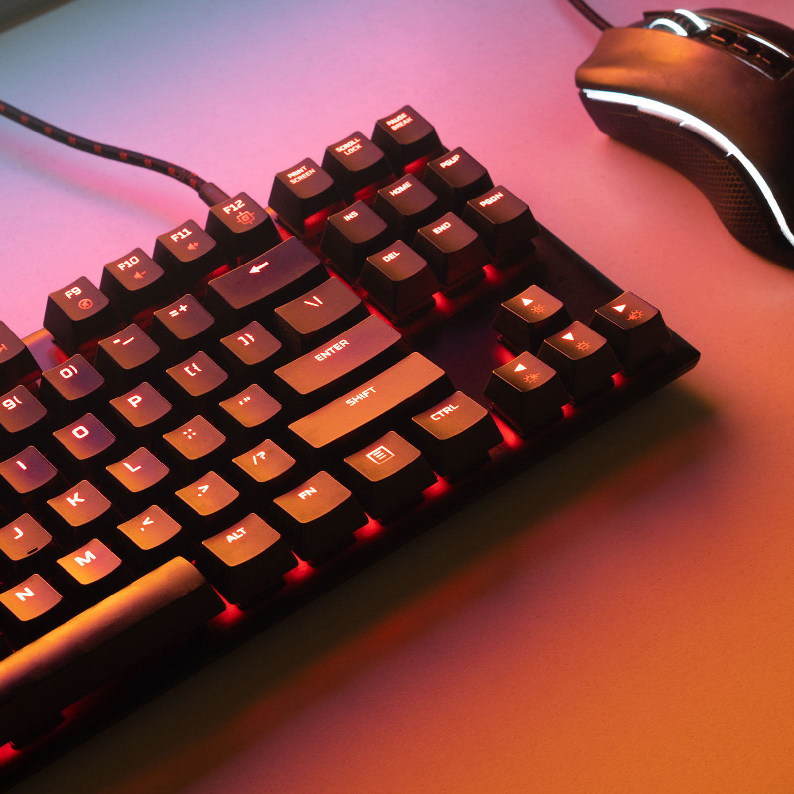 Un teclado de juego negro con retroiluminación roja y un ratón de juego a juego en una superficie iluminada.