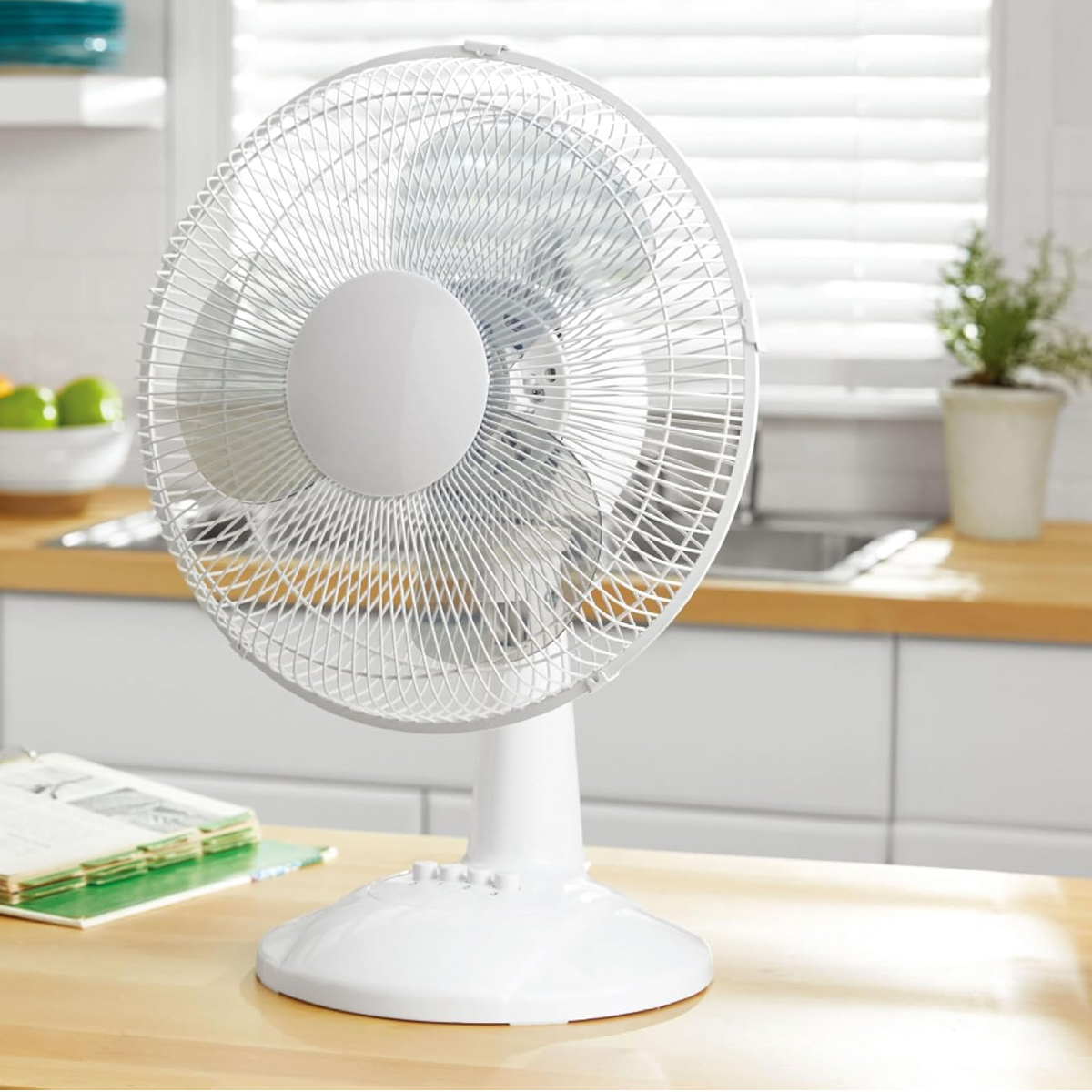 Ein weißer Tischventilator steht auf einer Holztheke in einer Küche mit weißem Hintergrund.