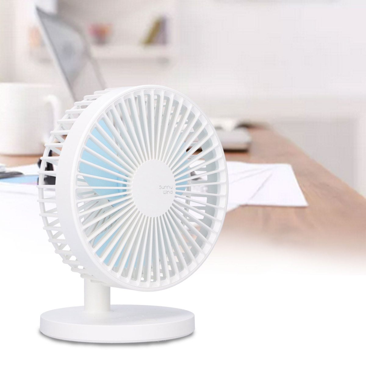 Kleiner weißer Tischventilator mit blauen Rotorblättern auf einem Holztisch in einem hellem Büro.
