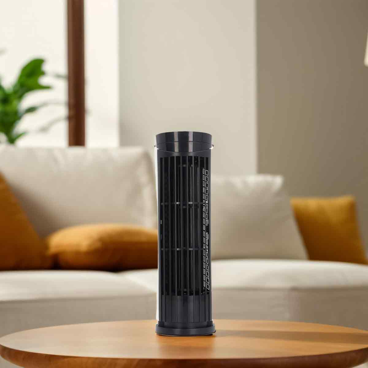 Ein schwarzer Turmventilator steht auf einem Holztisch vor einem weißen Sofa mit gelben Kissen in einem hellen Wohnzimmer.