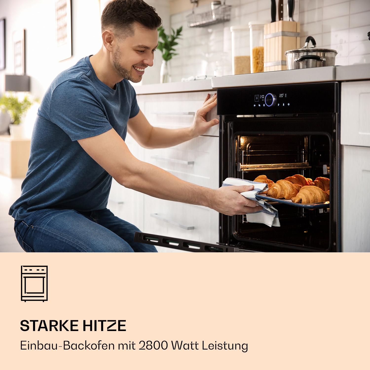 Ein smiling Mann nimmt frisch gebackene Croissants aus einem modernen schwarzen Einbau-Backofen in einer Küche.