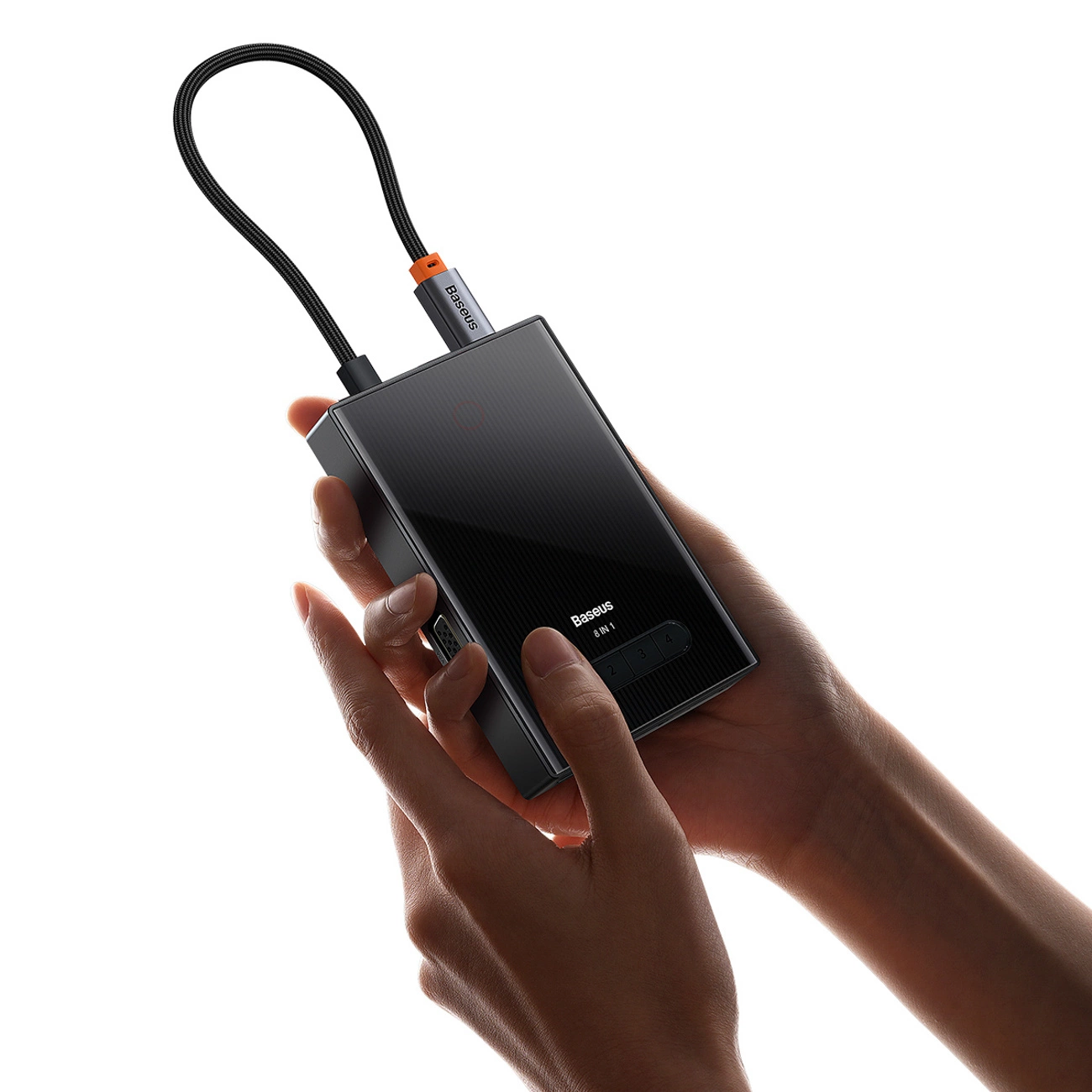 Mani che tengono un hub USB-C Baseus 8-in-1 nero con cavo su sfondo bianco.