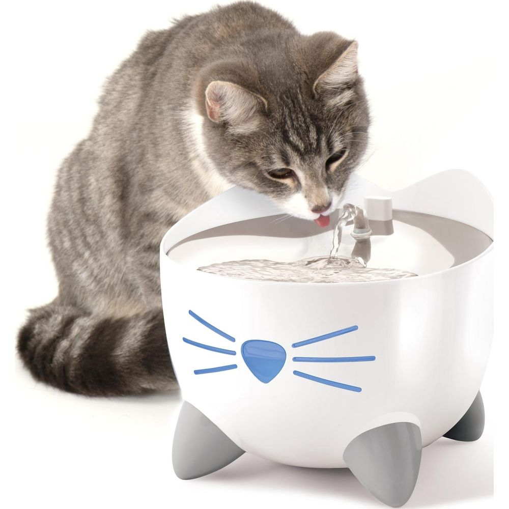 Un gato atigrado gris bebe de una fuente de agua blanca para gatos con bigotes azules.