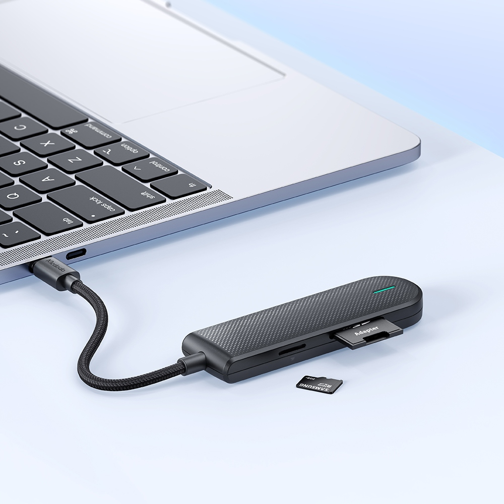 Un hub USB-C nero con una scheda SD inserita è collegato tramite cavo a un computer portatile argento.