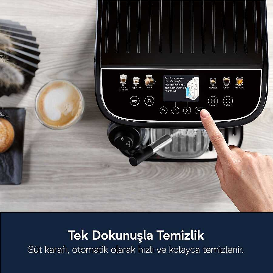Hand berührt das Display eines schwarzen Kaffeevollautomaten neben einer Tasse Cappuccino auf Holz.