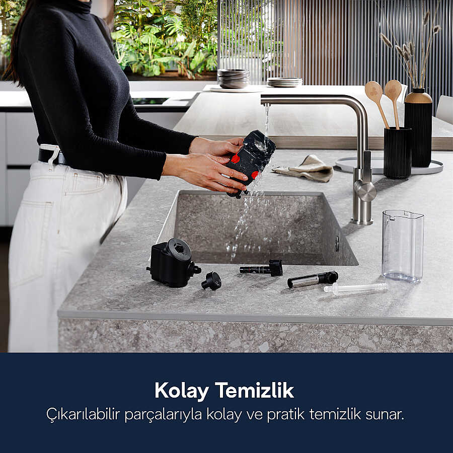 Bir kadın modern mutfaktaki evyede cihazın çıkarılabilir parçalarını yıkıyor.