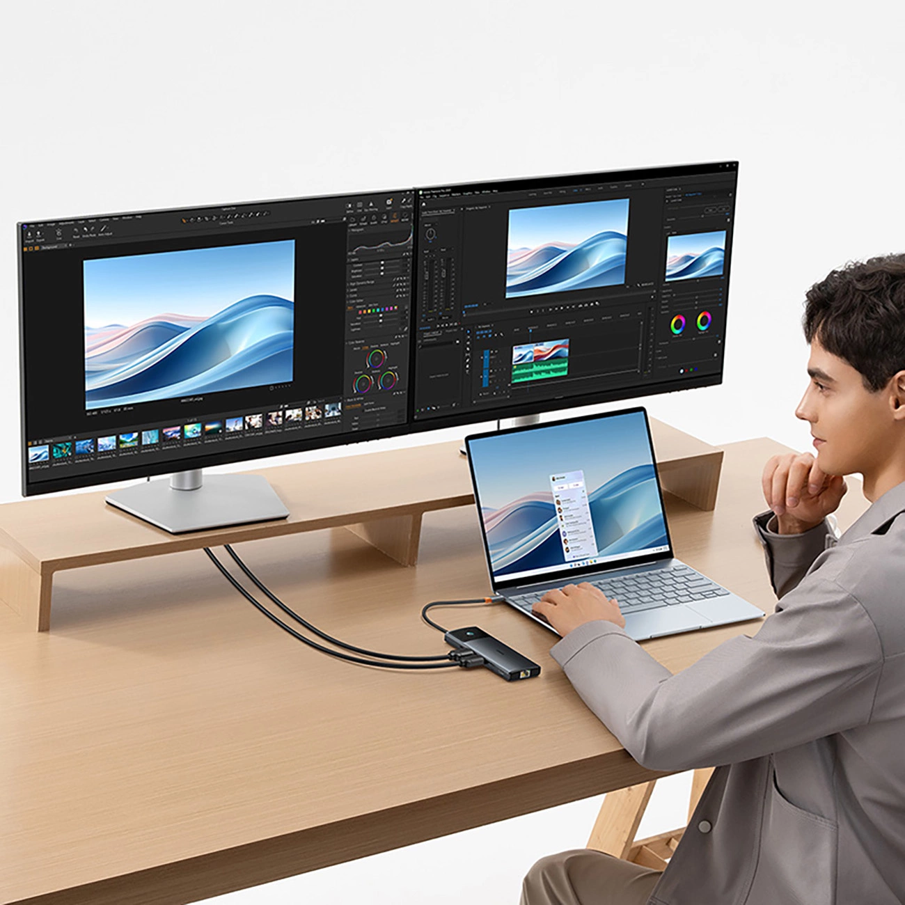 Un uomo usa un portatile collegato a due grandi monitor e un hub su una scrivania.
