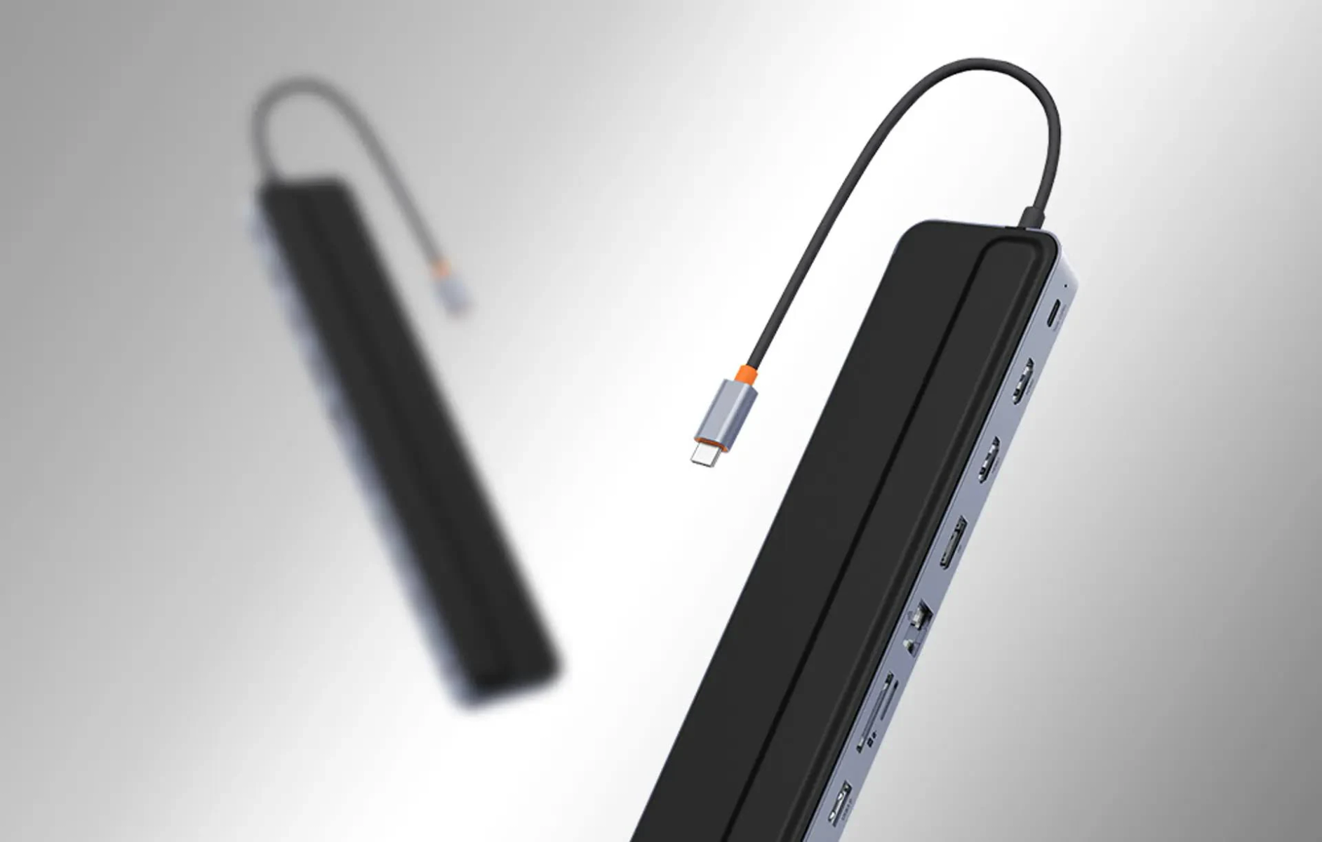 Un lungo hub USB-C nero e argento con varie porte fluttua su sfondo grigio.