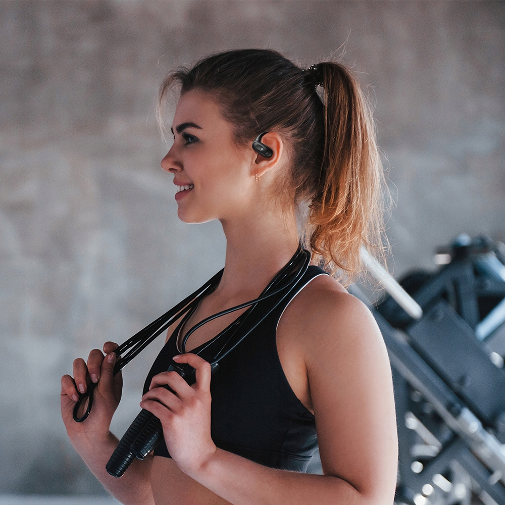 Una donna sorridente in abbigliamento sportivo tiene una corda per saltare in palestra, con auricolari neri.