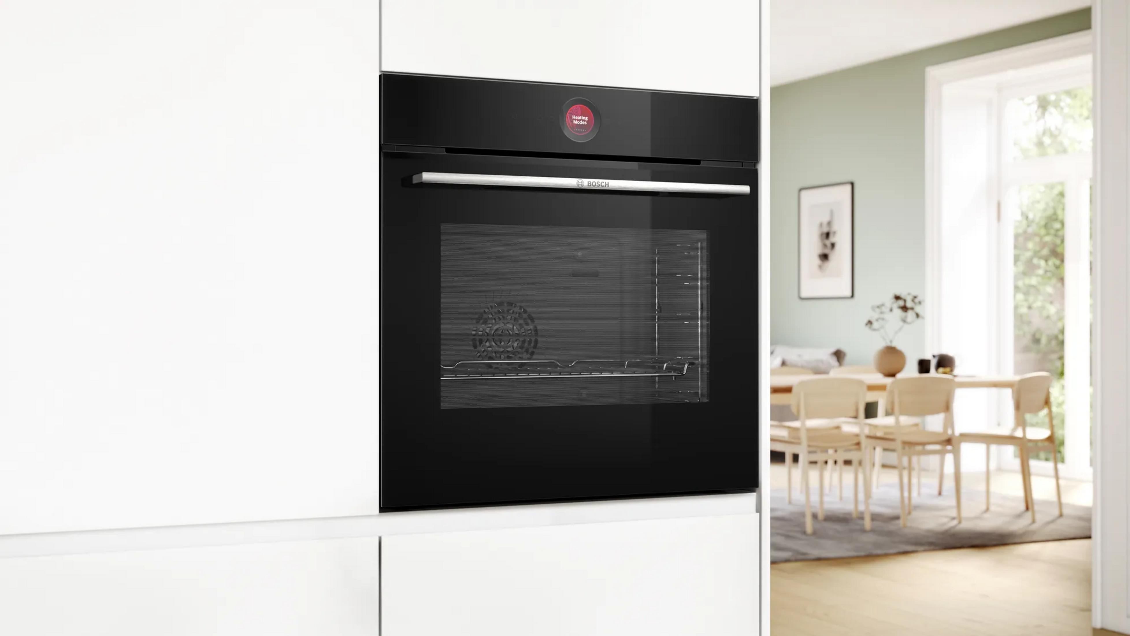 Un four encastrable Bosch noir installé dans un meuble de cuisine blanc, avec une salle à manger lumineuse en arrière-plan.