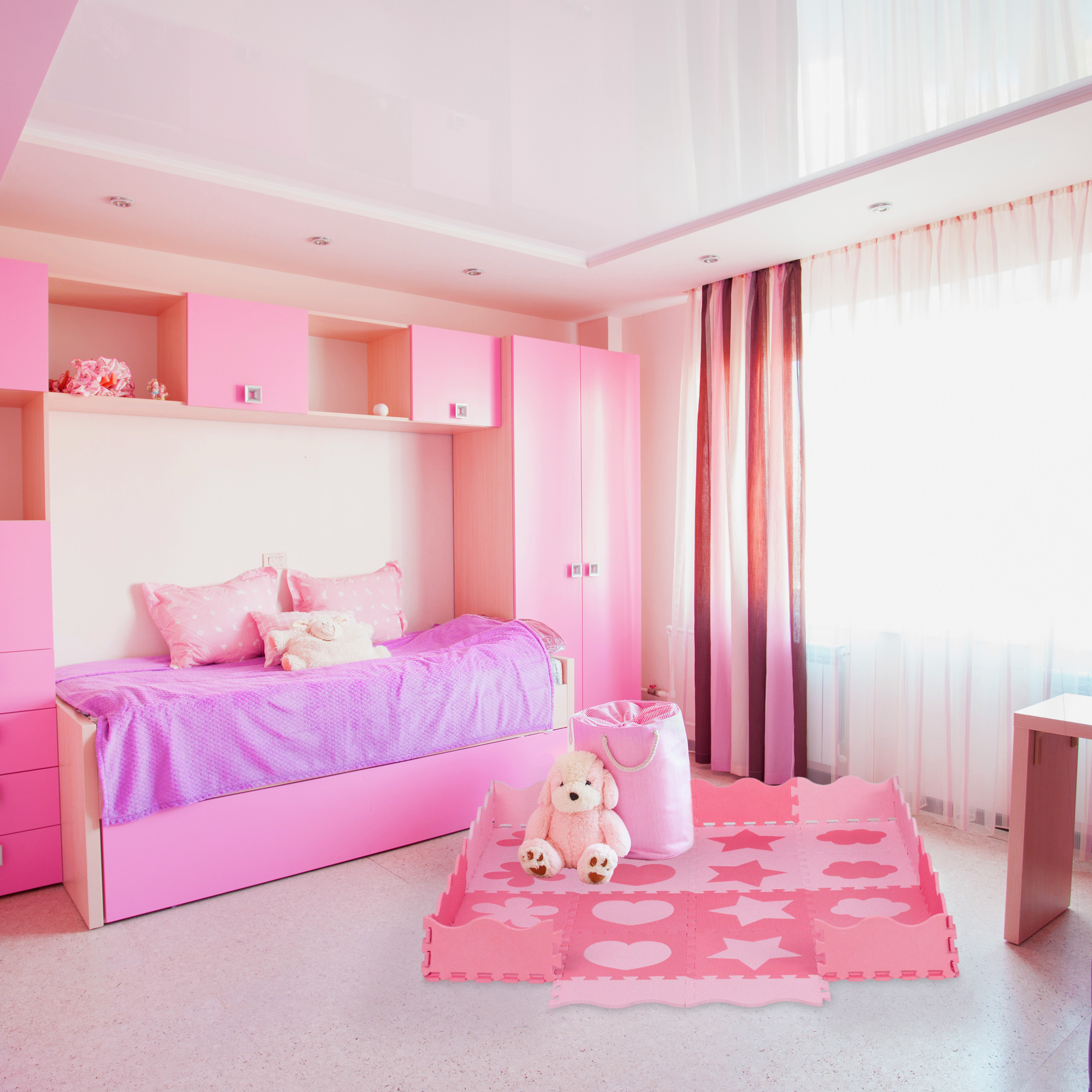 Ein hellrosa Kinderzimmer mit einem Bett mit lila Bezug, Schränken und einer rosa Spielmatte auf dem Boden.