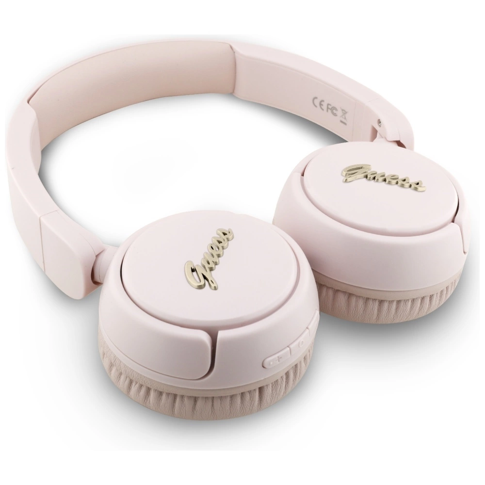 Cuffie wireless rosa chiaro con logo Guess dorato su sfondo bianco.