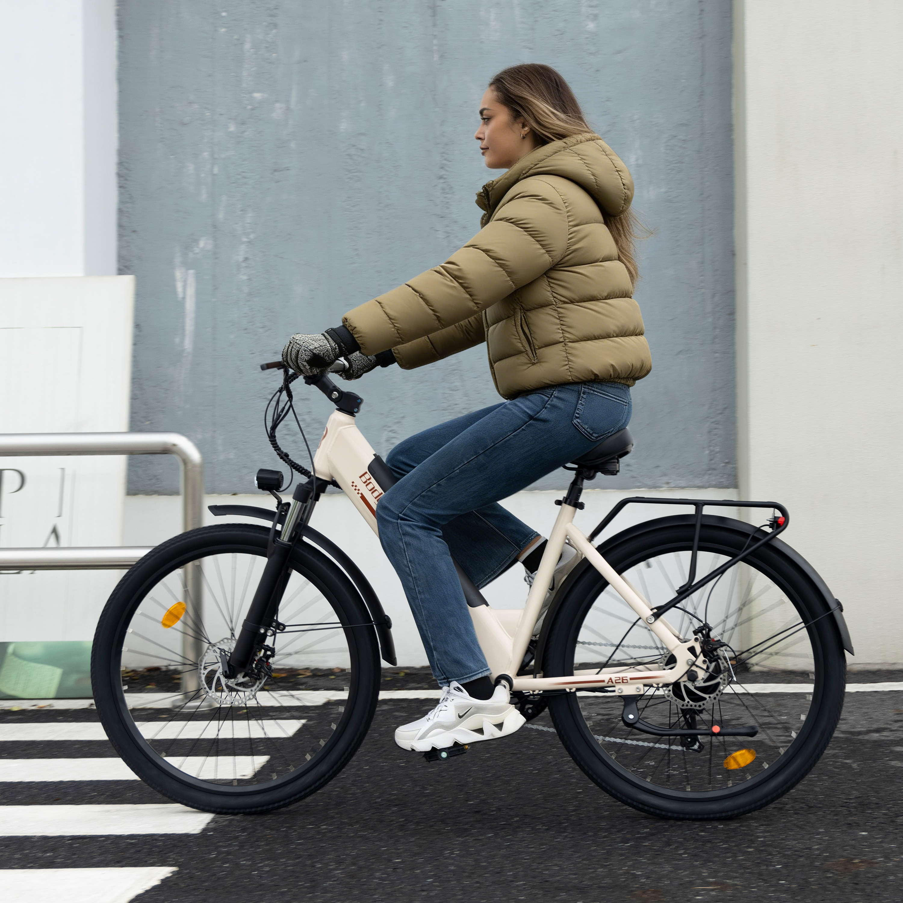 Eine Frau in olivgrüner Jacke und Jeans fährt ein beiges Elektrofahrrad.