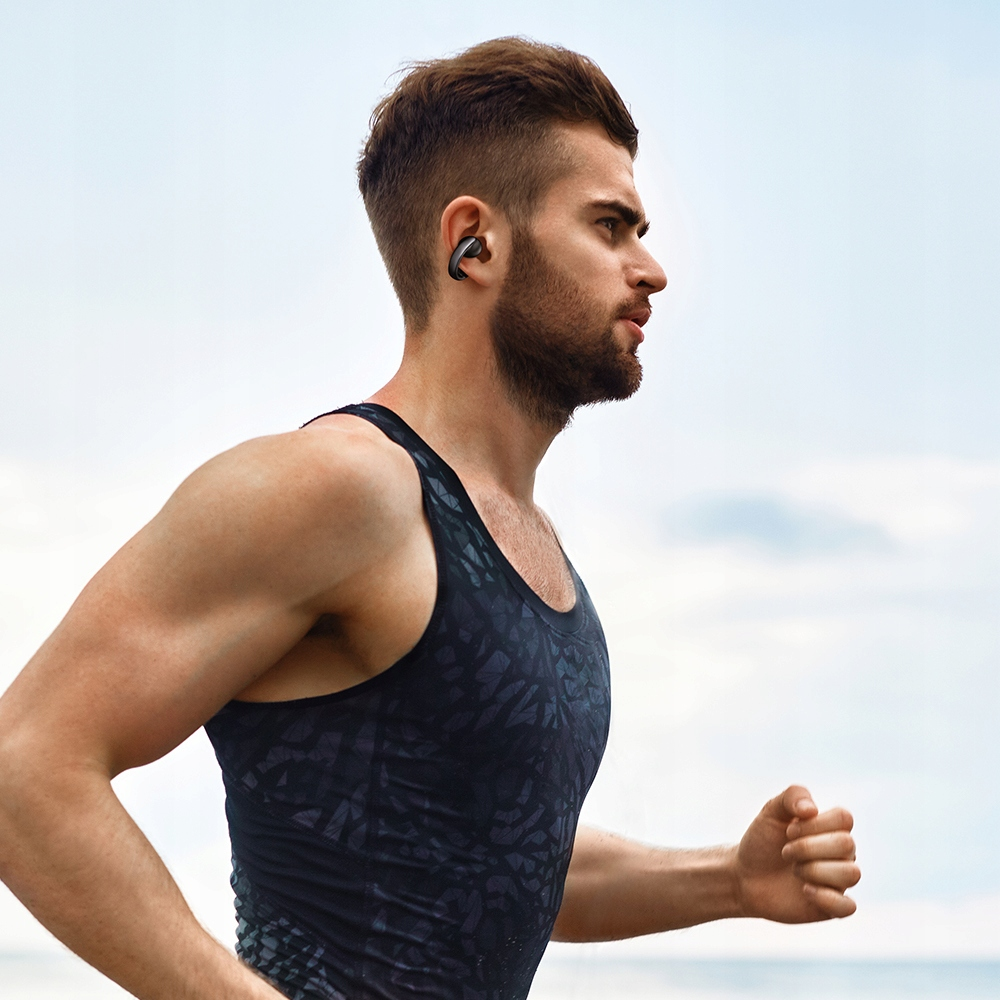 Un uomo con canotta nera e auricolari wireless corre all'aperto.