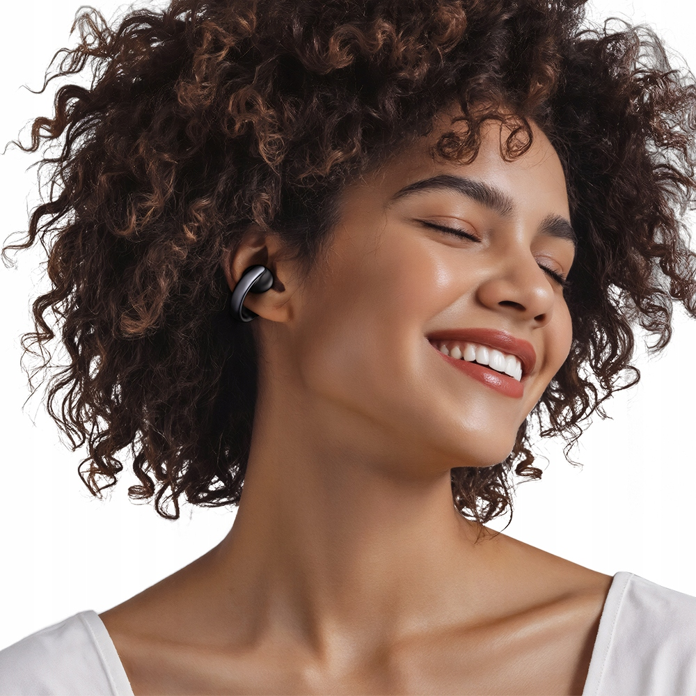 Una giovane donna con capelli castani ricci sorride felice a occhi chiusi, indossando un auricolare nero.