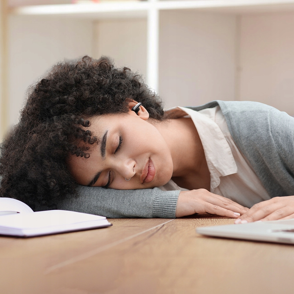 Una donna dorme su un tavolo di legno con un libro e un laptop.