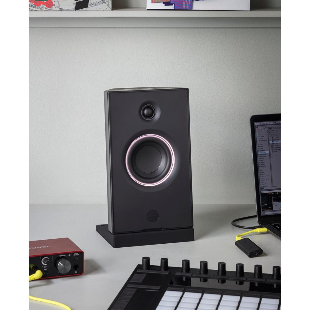 Un moniteur de studio noir avec un anneau lumineux posé sur un bureau près d'un équipement audio.