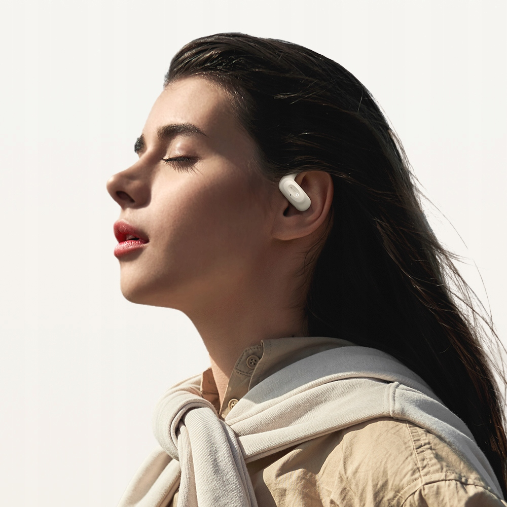 Profilo di una donna con capelli scuri e occhi chiusi, che indossa un auricolare wireless bianco su sfondo bianco.
