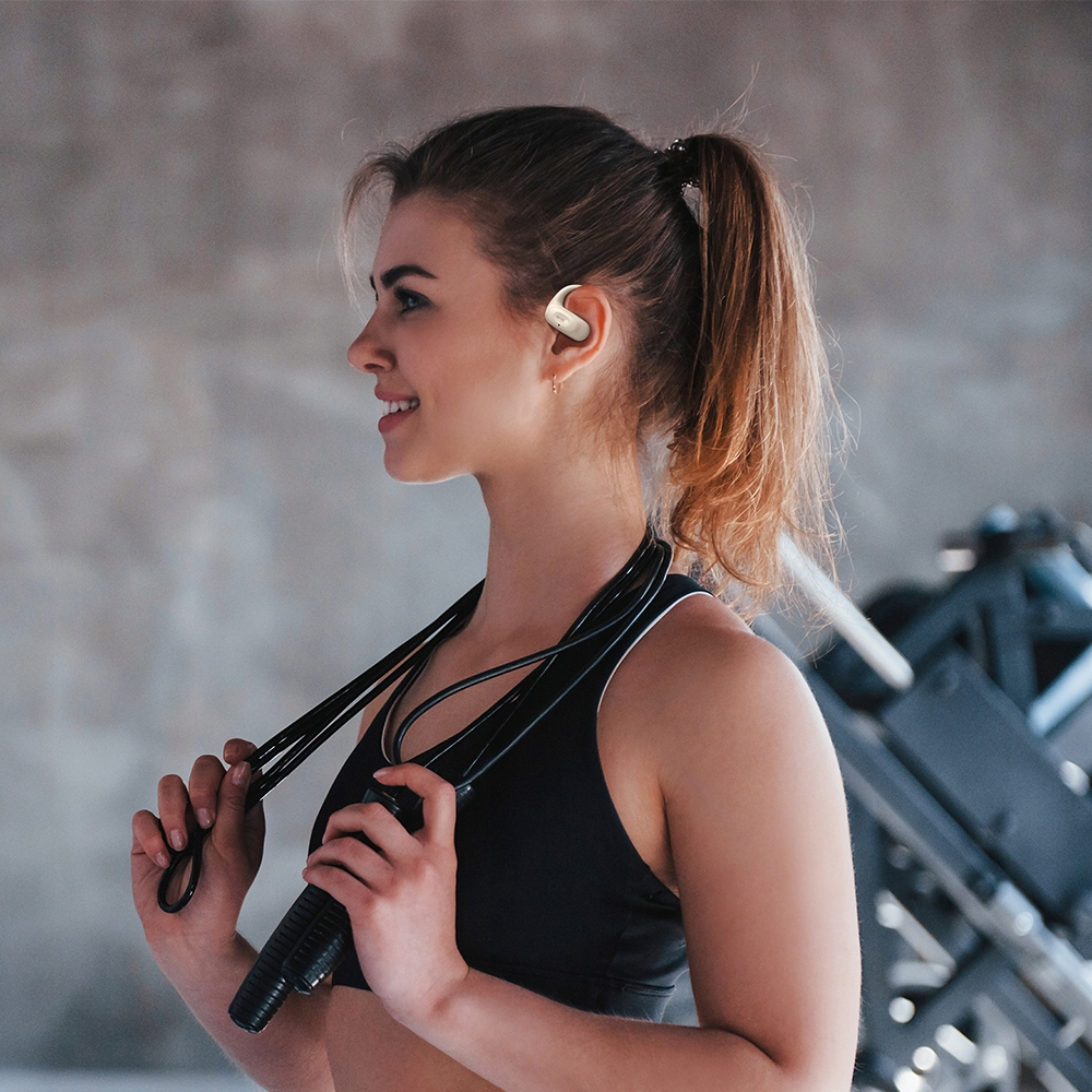 Una donna sportiva con i capelli raccolti tiene una corda per saltare e indossa auricolari bianchi in palestra.