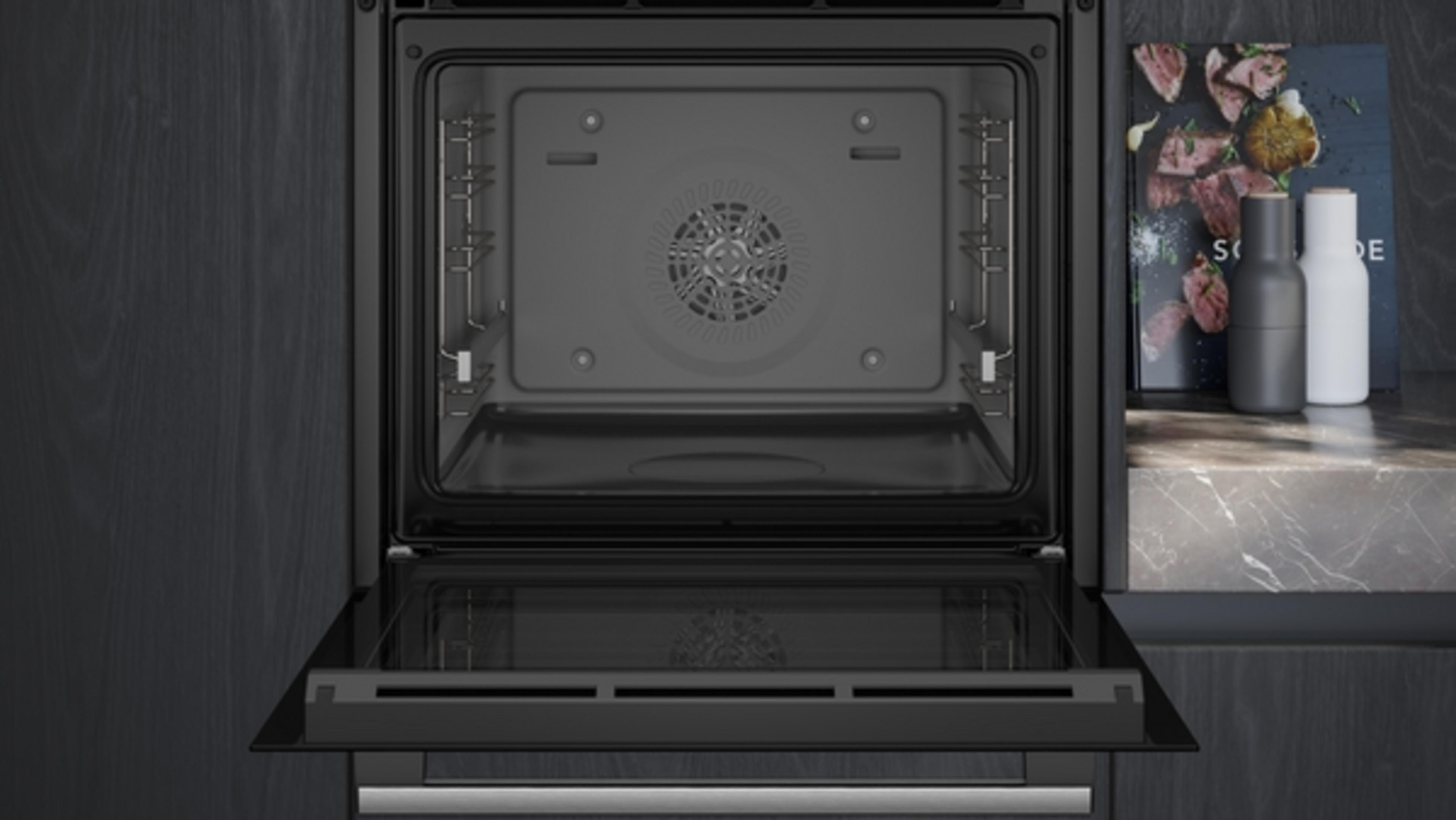 Un four noir ouvert avec un intérieur vide, un ventilateur et une porte ouverte contre un mur en bois sombre.