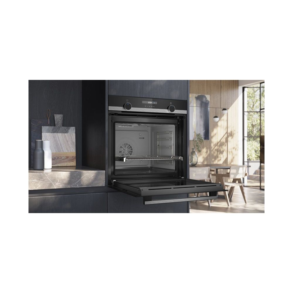 Cuisine moderne avec un four noir encastré, porte ouverte, devant un coin repas lumineux à l'arrière-plan.