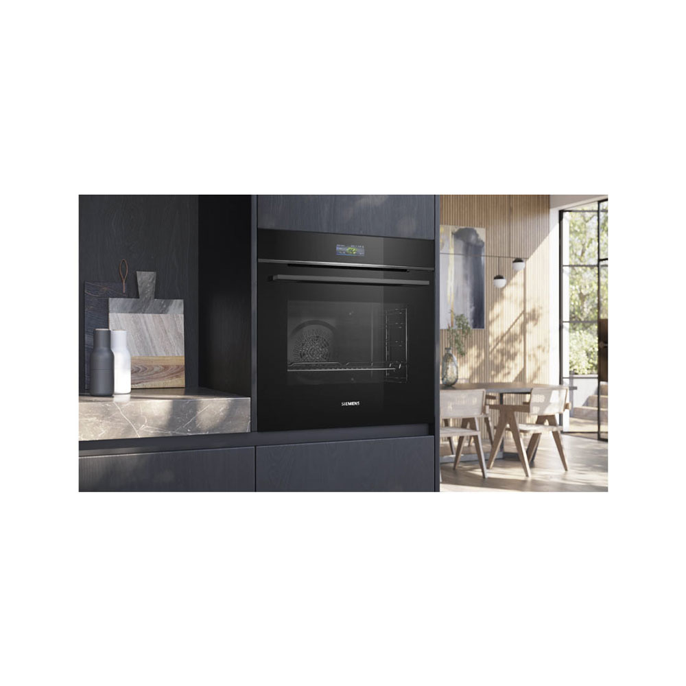 Un four encastrable noir dans un meuble de cuisine sombre, avec un coin repas en arrière-plan.