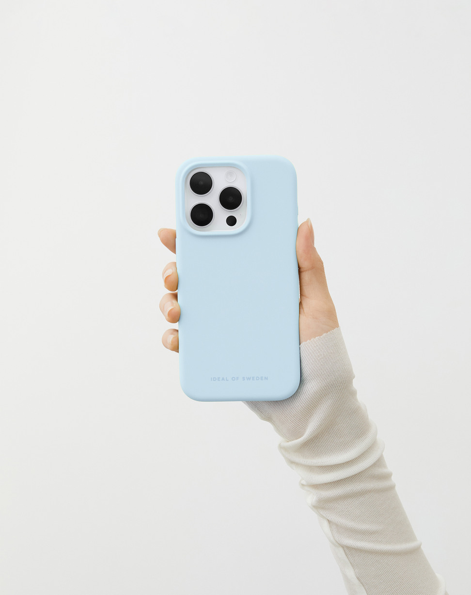 Eine Hand in einem weißen Pullover hält ein hellblaues Smartphone gegen einen weißen Hintergrund.
