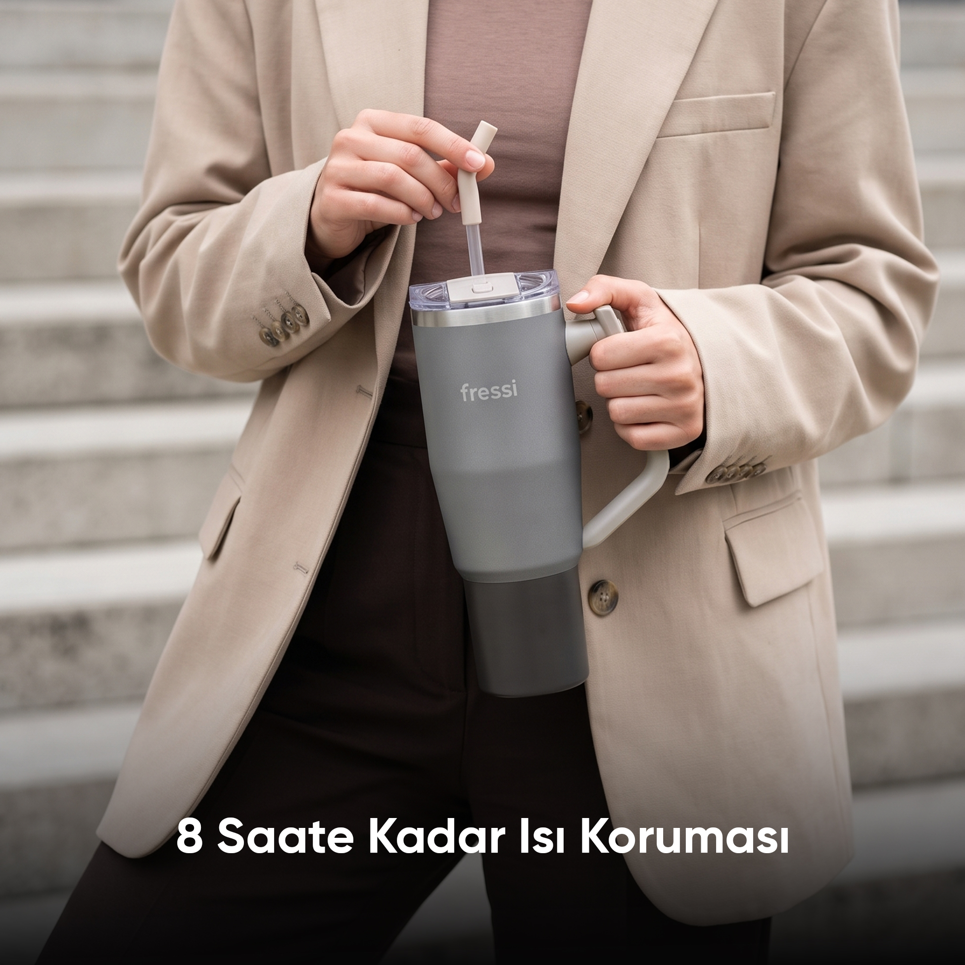 Bej ceketli bir kişi taş merdivenler önünde pipetli büyük gri bir fressi bardak tutuyor.