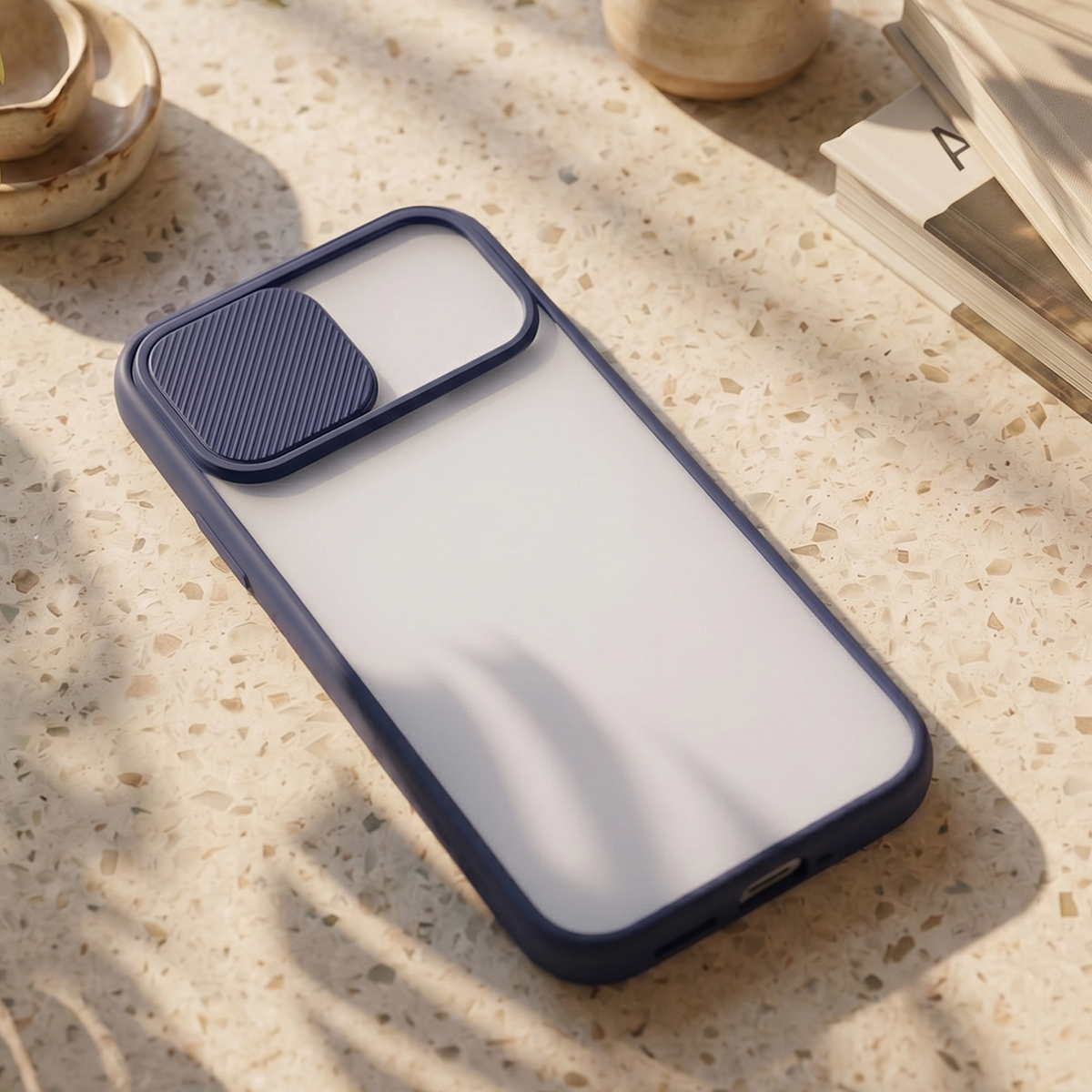 Blaue Smartphone-Hülle mit Kameraabdeckung auf einem gesprenkelten Steintisch mit Büchern.