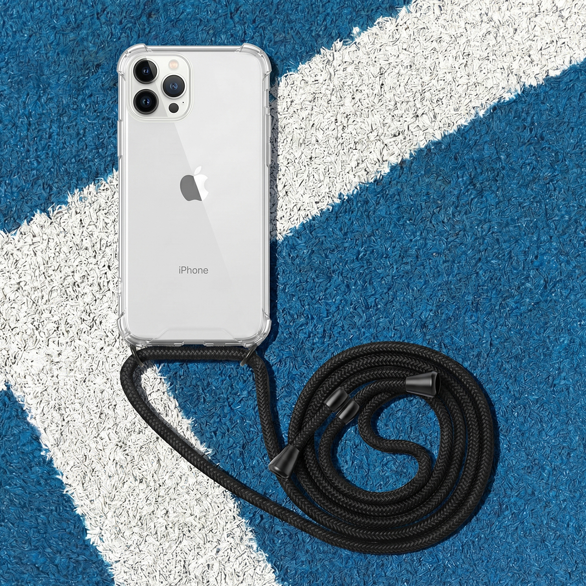 Un iPhone blanco en funda transparente con cordón negro yace sobre un campo deportivo azul con líneas blancas.