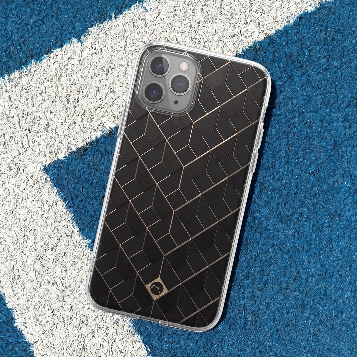 Smartphone in custodia trasparente con motivo geometrico nero e oro su erba sintetica blu.
