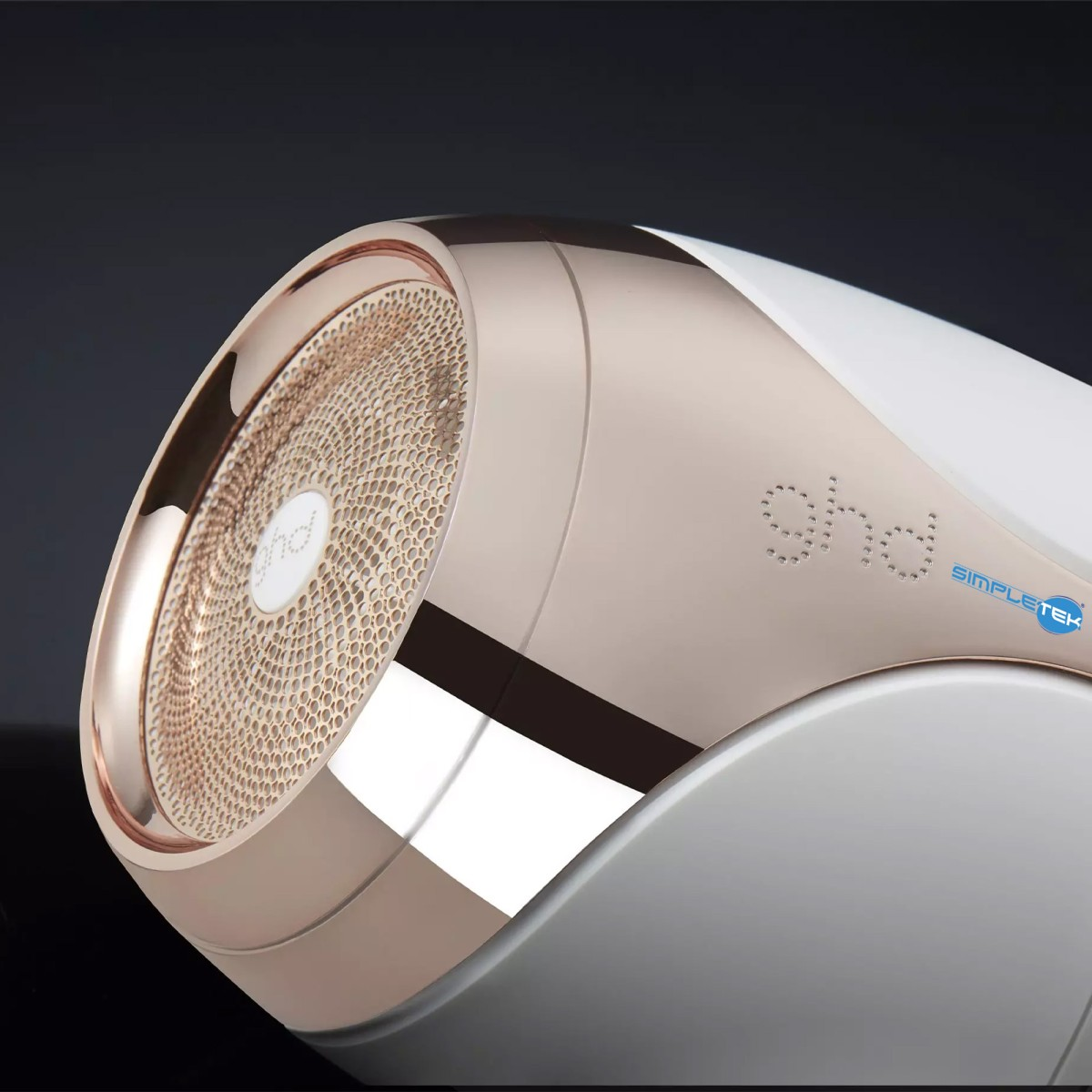 Primo piano di un asciugacapelli ghd bianco e oro rosa con griglia lavorata su sfondo scuro.
