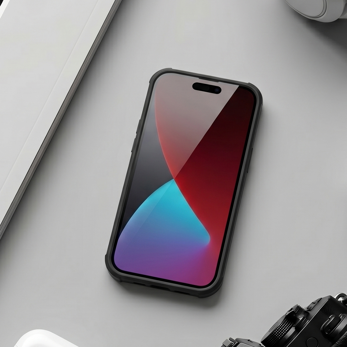 Uno smartphone in custodia nera poggia su una superficie grigia vicino a un taccuino bianco e a una fotocamera.