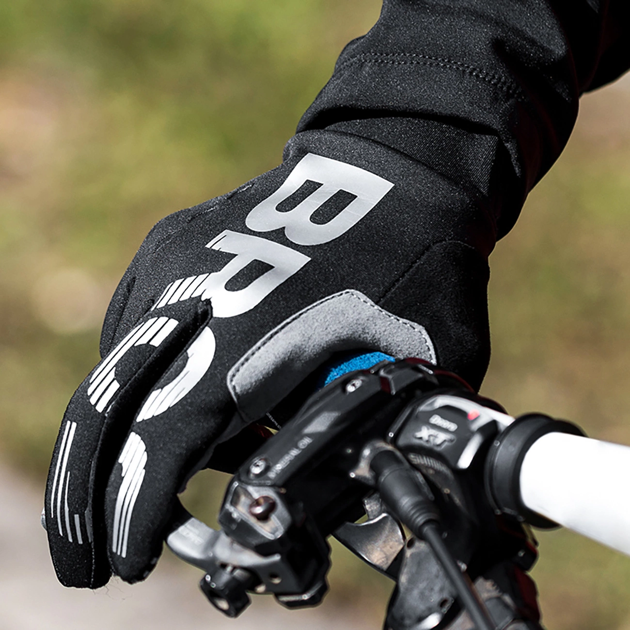 La mano di un ciclista con un guanto nero e scritte bianche afferra il manubrio.