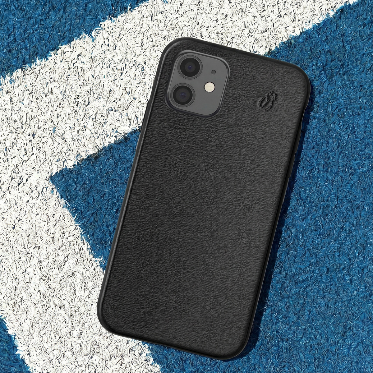 Una cover per smartphone in pelle nera con doppia fotocamera giace su una superficie blu e bianca.