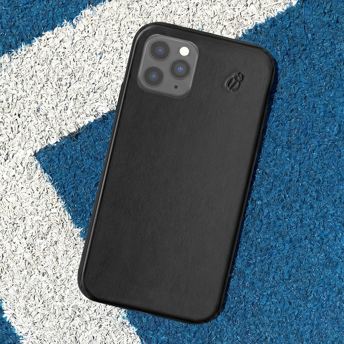 Uno smartphone nero con custodia si trova su un campo sportivo blu e bianco.