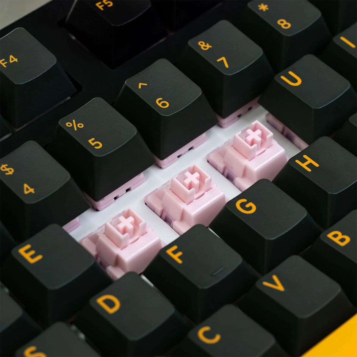 Sarı harfli siyah klavye tuşları ve ortada görünen pembe mekanik anahtarlar.